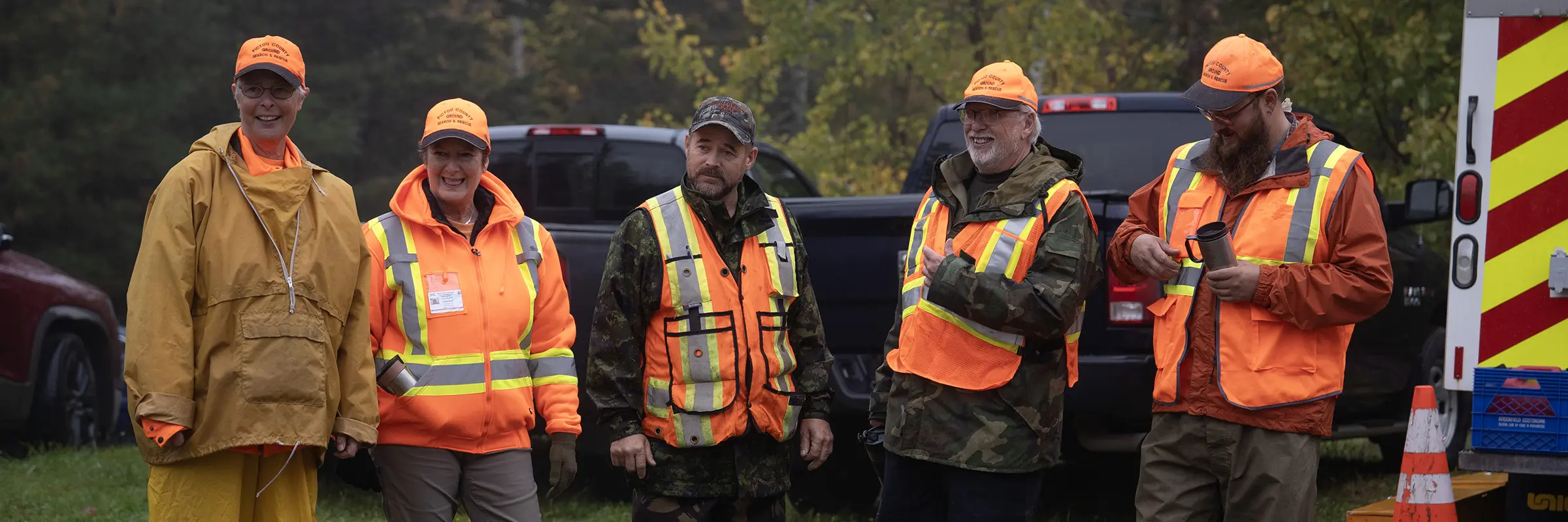 A group of five people are standing and smiling. They are all wearing bright orange.