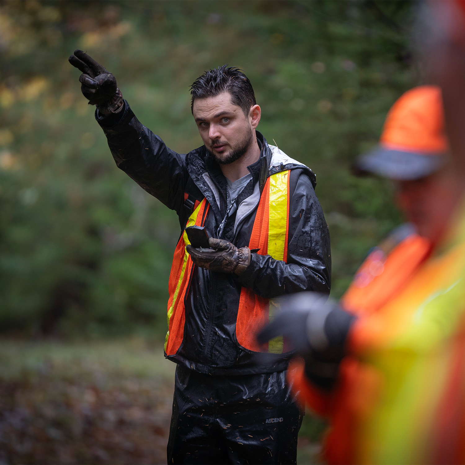 A man holding a compass pointing two fingers while looking at another person standing next to the camera.